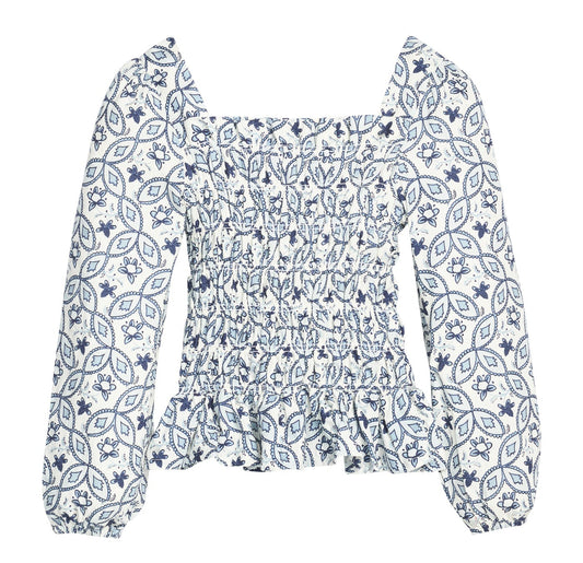 A long-sleeve smocked blouse with a blue and white floral and geometric pattern, featuring a square neckline and a ruffled peplum hem.